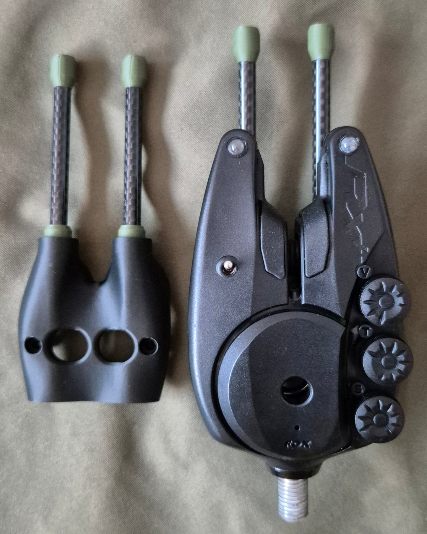 Two black fishing reel components on a beige fabric background